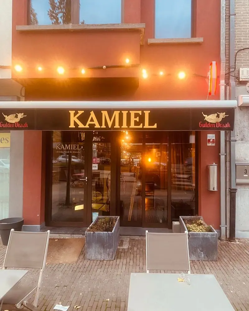 De terracottakleurige gevel van Kamiel in het late licht, met de gele letters KAMIEL onder de luifel en een snoer lichtjes.