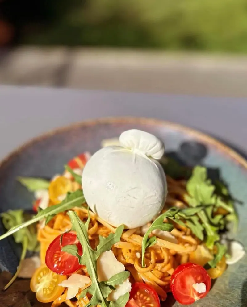 Pasta met een bol burrata, kerstomaatjes en rucola in een blauwgrijze kom.