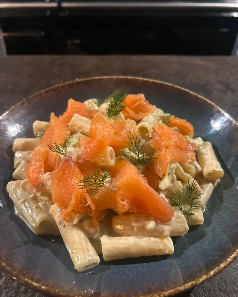 Rigatoni met zachte kaassaus en gerookte zalm op een blauwgrijs bord.
