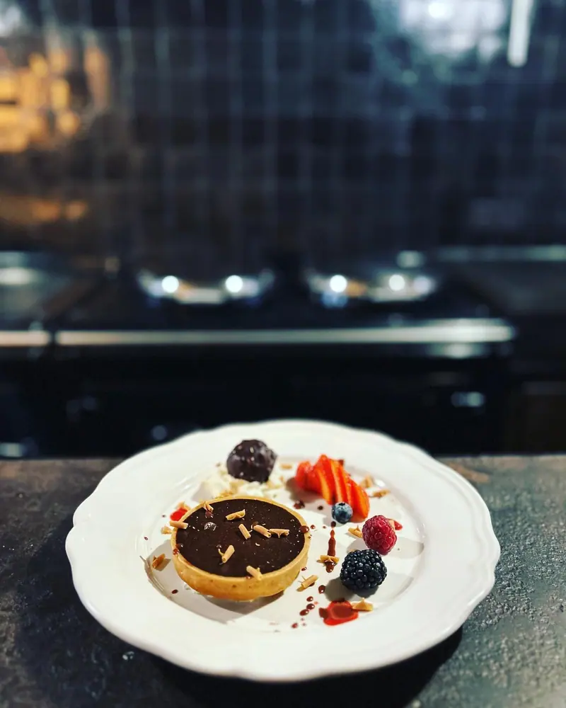 Een chocoladetaartje met rood fruit en room op een wit bord.
