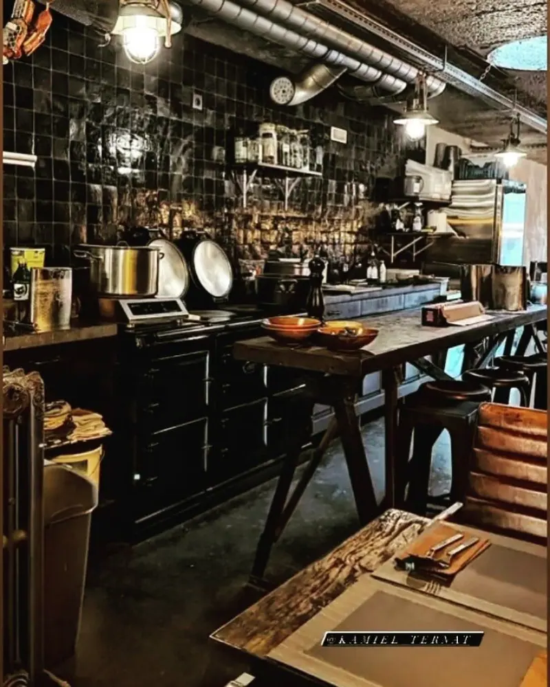 De zwarte tegelwand van de keuken met een hanglamp en een werktafel.