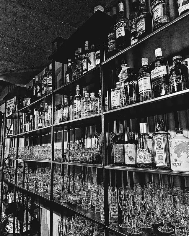 Zwart-witfoto van de rekken achter de bar met flessen en glazen.