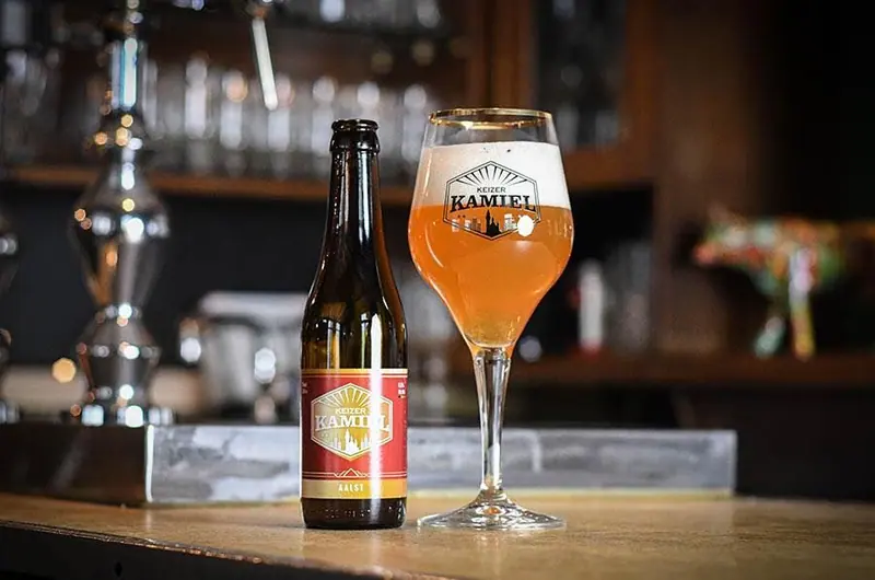 Een flesje en een glas amberkleurig bier op de bar.