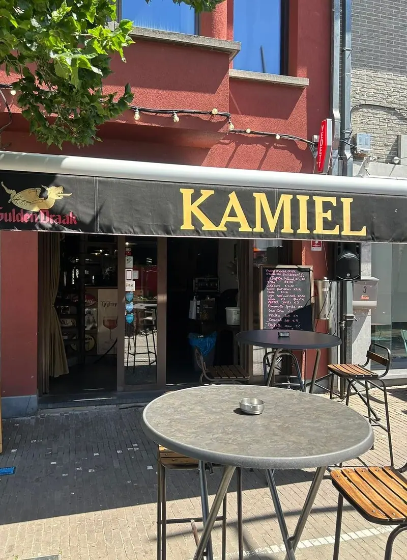 De gevel van Kamiel met de luifel, een krijtbord en een hoge tafel ervoor.
